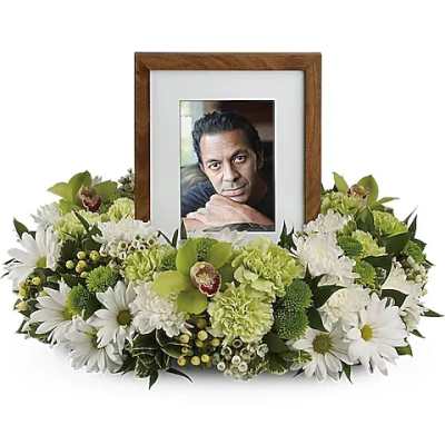 Framed photo surrounded by white and green funeral flowers