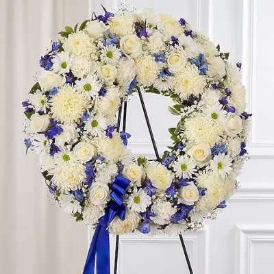 White and blue floral wreath on a black stand with a blue ribbon