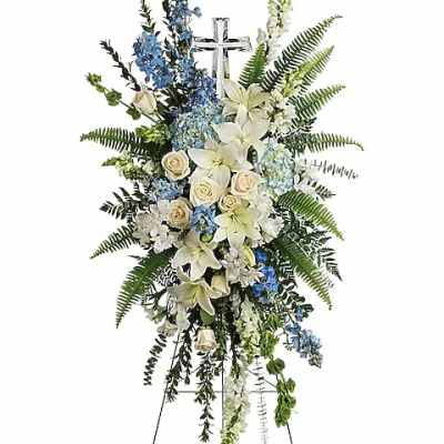 Standing funeral spray with white lilies, roses, and blue flowers on an easel