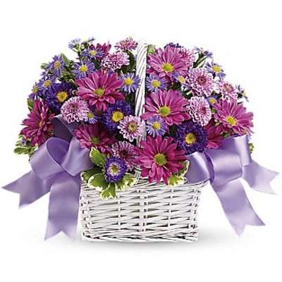 Purple and pink mixed flowers in a white wicker basket with lavender ribbon