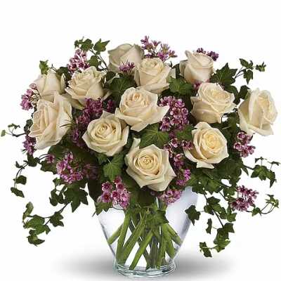 Cream roses and purple filler flowers in a clear glass vase