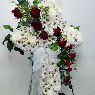 Cross-shaped floral spray with red roses and white daisies tied with a white bow