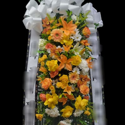 Tall standing floral spray with orange and yellow blooms and a large white bow