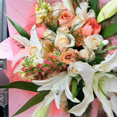 Bouquet of white lilies and peach roses wrapped in pink paper