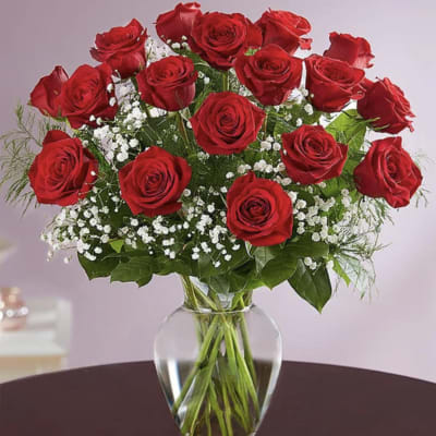 Dozen red roses with white filler flowers arranged in a clear glass vase