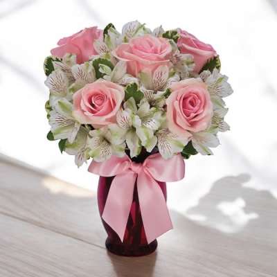 Pink roses and white alstroemeria in a red glass vase with a pink satin bow