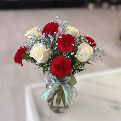Red carnations and white roses in a glass vase with a ribbon
