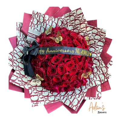 Red rose bouquet wrapped in pink Dior-pattern paper with a black ribbon