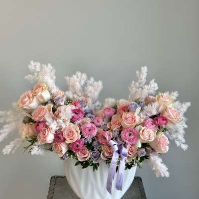 Pink and lavender roses arranged in a white vase with fluffy white accents