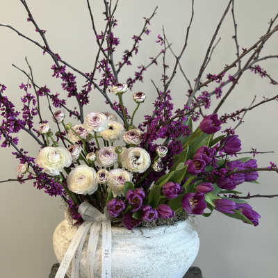 Purple tulips and white ranunculus in a textured vase with branches