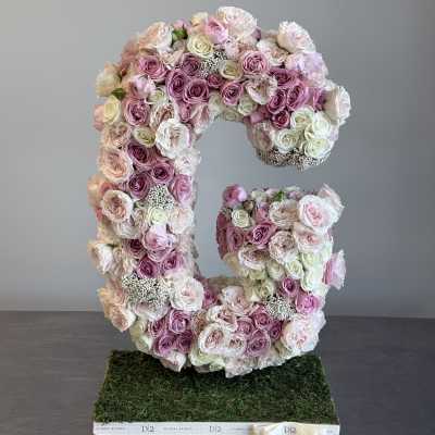 Large floral letter C made of pink and white roses on a moss base
