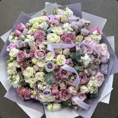 Large pastel bouquet of roses and white blooms wrapped in lavender paper