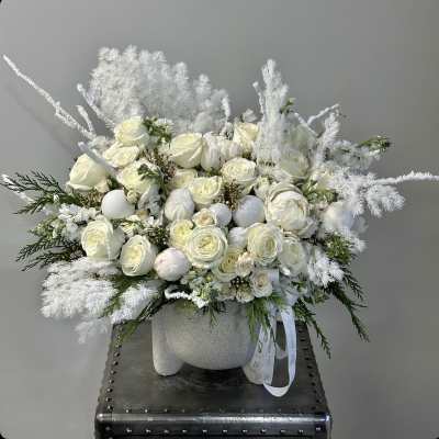 White rose arrangement in a textured vase with feathery white accents