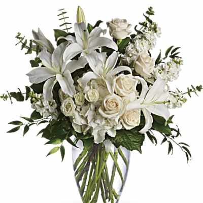 Tall arrangement of white lilies, roses, and other white flowers in a clear glass vase