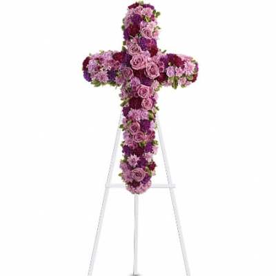 Standing floral cross of pink and purple blooms on a white metal easel.