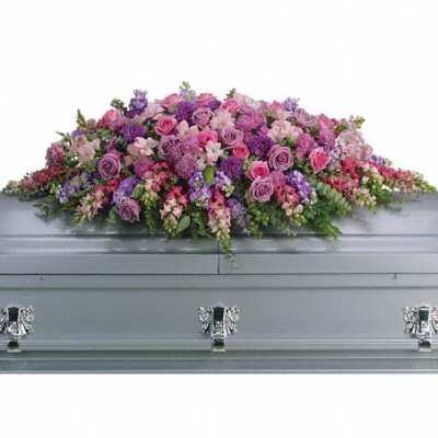 Long pink and purple mixed flower casket spray arranged on top of a gray casket