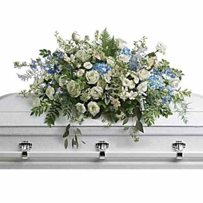 White and blue floral casket spray arranged across a white casket top