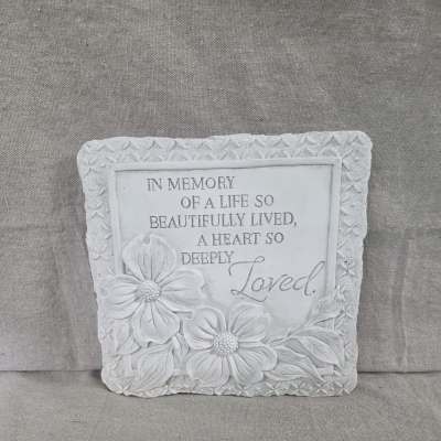 Square white memorial stone plaque with carved flowers and the inscription In Memory of a Life So Beautifully Lived.