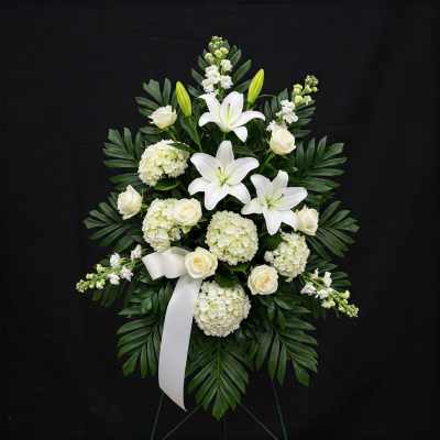 White lilies and roses in a standing spray with a white ribbon