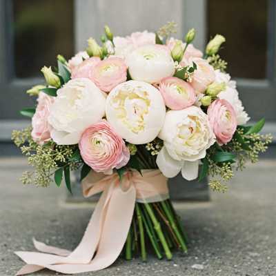 Blush and white bouquet of peonies and ranunculus tied with a pale ribbon