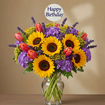 Bright bouquet of sunflowers, tulips, and purple flowers in a glass vase