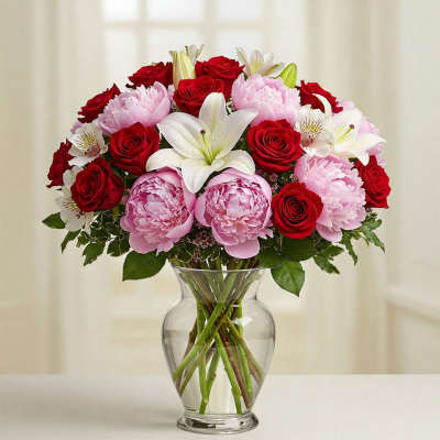 Bouquet of red roses, pink peonies, and white lilies in a clear glass vase
