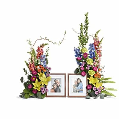 Pair of tall, colorful floral arrangements framing two wooden photo frames with portraits.