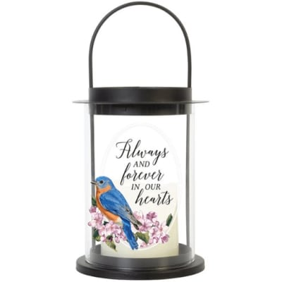 Black metal lantern with memorial quote, bluebird, and pink blossoms around a white candle.