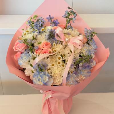 Bouquet of pink roses, white daisies, and blue flowers wrapped in pink paper