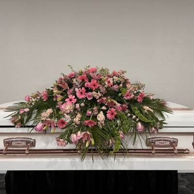 Pink floral spray arranged on top of a white casket