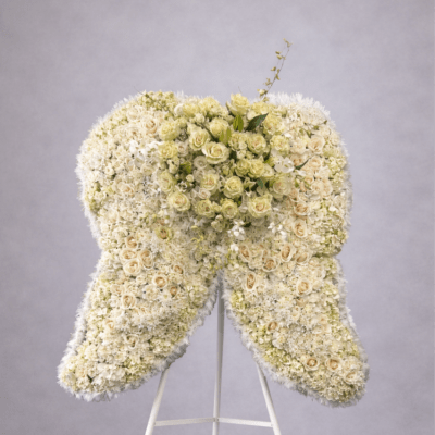 Large standing arrangement of white and cream flowers shaped like angel wings on a white easel.