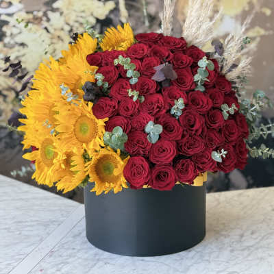 Red roses and yellow sunflowers in a black round box