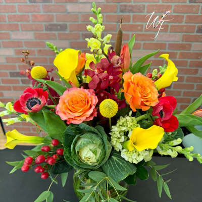 Bright mixed bouquet with orange roses, yellow calla lilies, and red blooms in a glass vase