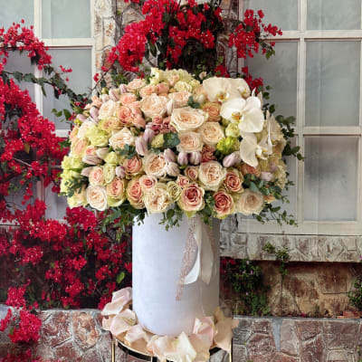 Large pastel rose arrangement with white orchids in a tall white vase