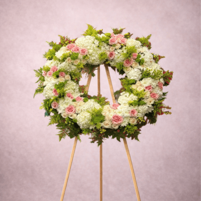 Standing wreath of white and pink flowers with green accents on a wooden easel.