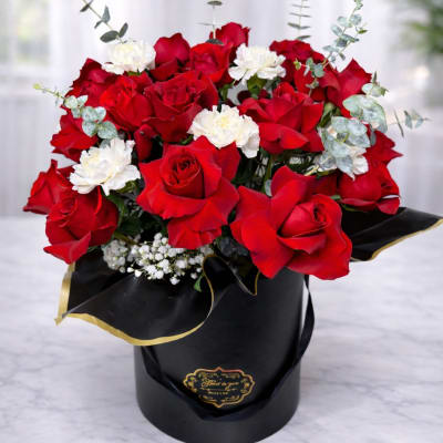 Red roses and white carnations arranged in a black hatbox