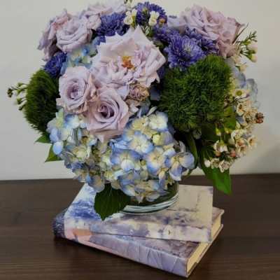 Lavender roses and blue hydrangeas arranged in a glass vase