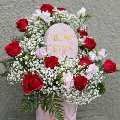 Red roses and pink flowers arranged around a pink memorial plaque
