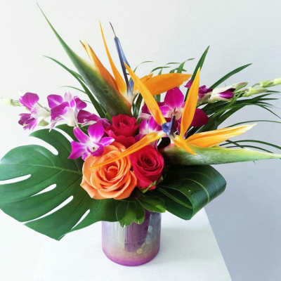 Tropical bouquet with roses, orchids, and bird of paradise in a glass vase