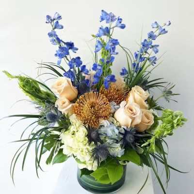 Mixed bouquet of blue, cream, and gold flowers in a glass vase