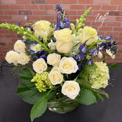 Cream roses and blue flowers arranged in a glass vase