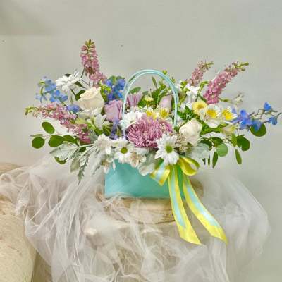 Pastel mixed flower arrangement in a turquoise basket with ribbon