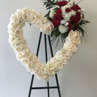 Heart-shaped floral wreath of white roses with a red rose cluster on an easel
