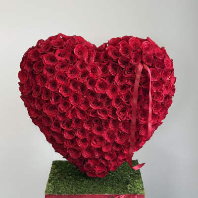 Heart-shaped arrangement of red roses on a moss-covered base with a ribbon