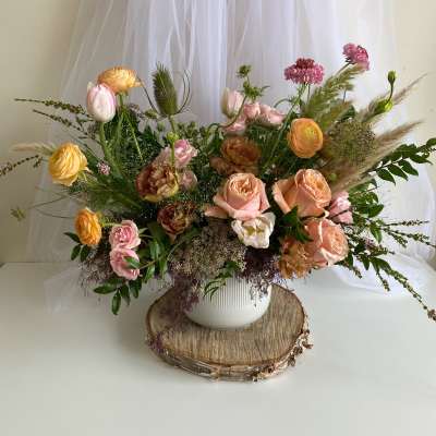 Mixed bouquet of peach, pink, and yellow flowers in a white vase
