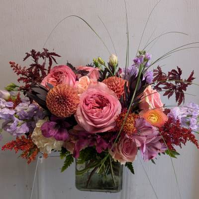 Low rectangular arrangement of pink roses, dahlias, and mixed blooms in a clear glass vase