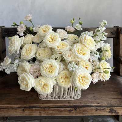 Cream roses and white blooms arranged in a wicker basket