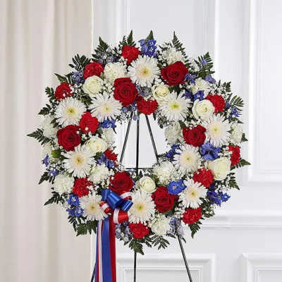 Red, white, and blue floral wreath on a black stand with ribbon