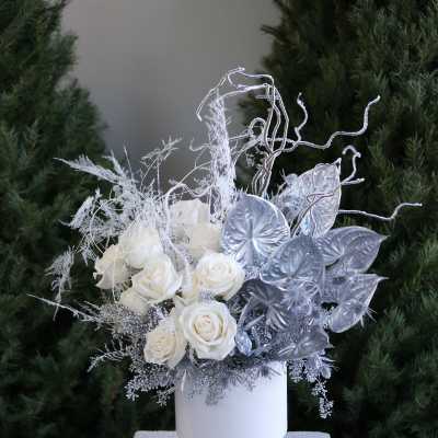 White roses in a white pedestal vase with silver decorative foliage