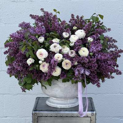 Large purple and white floral arrangement in a gray urn vase